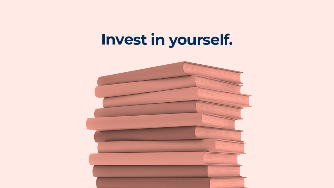A rosey-pink-hued stack of books appears on a pale blush pink background with the words "Invest in yourself" appearing in dark blue atop the bookstack